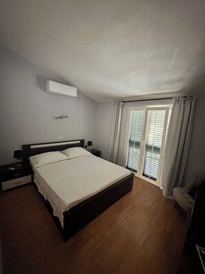 Un dormitorio con una cama grande, una mesita de noche, un estante en la pared y una ventana con persianas.