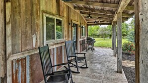 A covered porch with wooden walls, two rocking chairs, and a grill area. - Waterfront Missouri Escape w/ Private Pond & Dock! (Nevada)