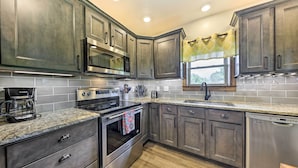 A modern kitchen with stainless steel appliances, granite countertops, and dark wood cabinets. - Waterfront Missouri Escape w/ Private Pond & Dock! (Nevada)