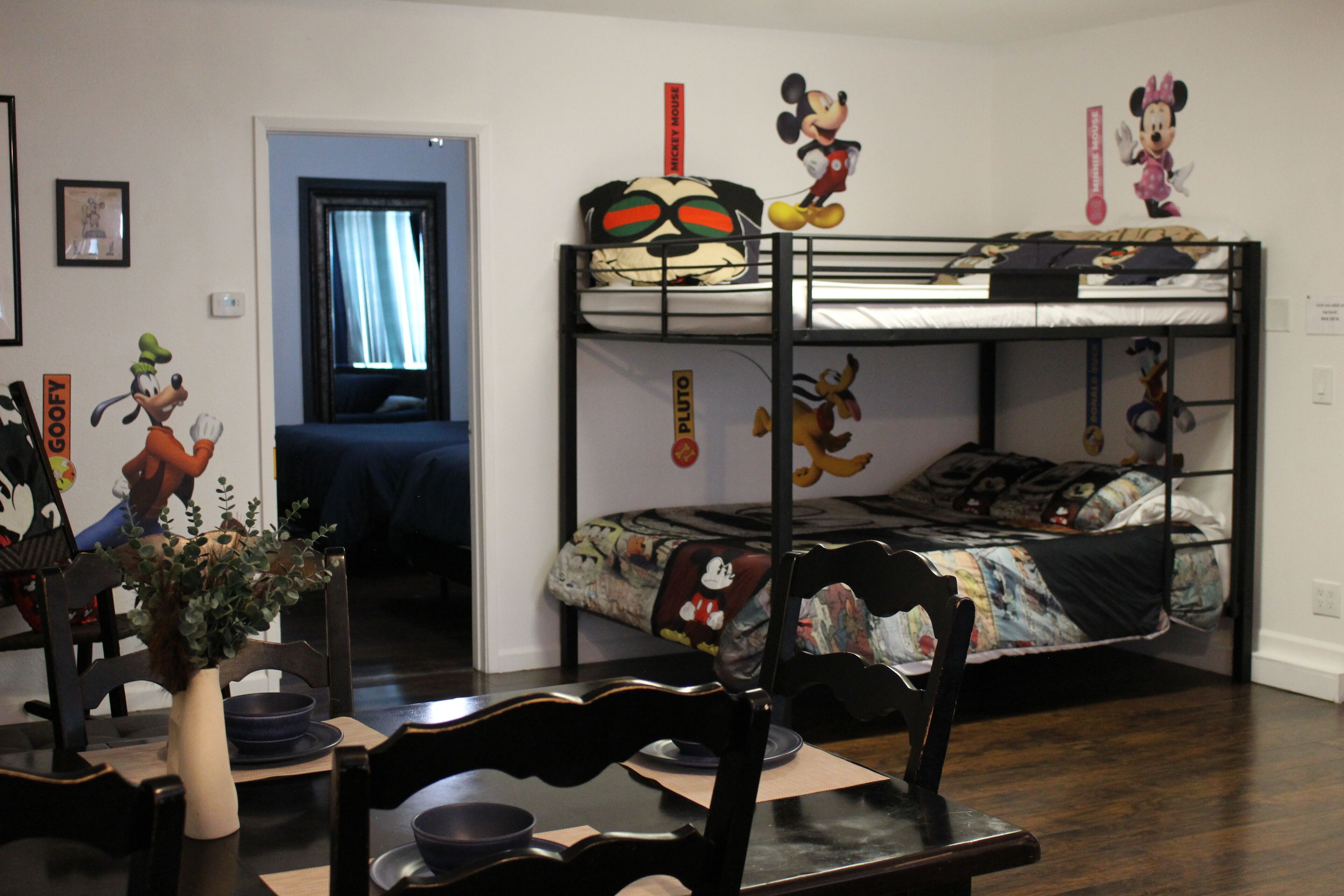 A room with bunk beds, a dining table, chairs, and a vase with flowers.