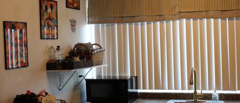 A kitchen with a microwave, sink, and window with blinds.