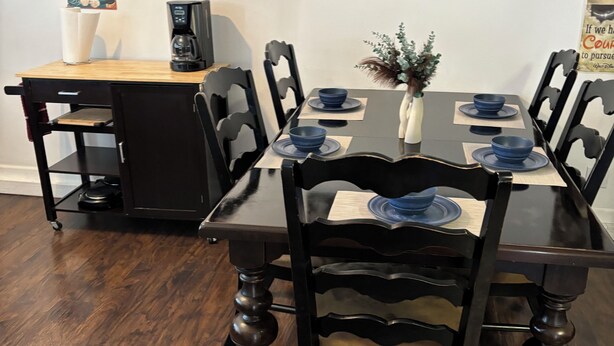 A dining area with a wooden table, black chairs, and a coffee machine.