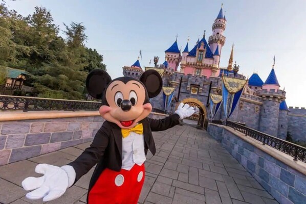 En person klædt ud som Mickey Mouse står foran en borglignende bygning.