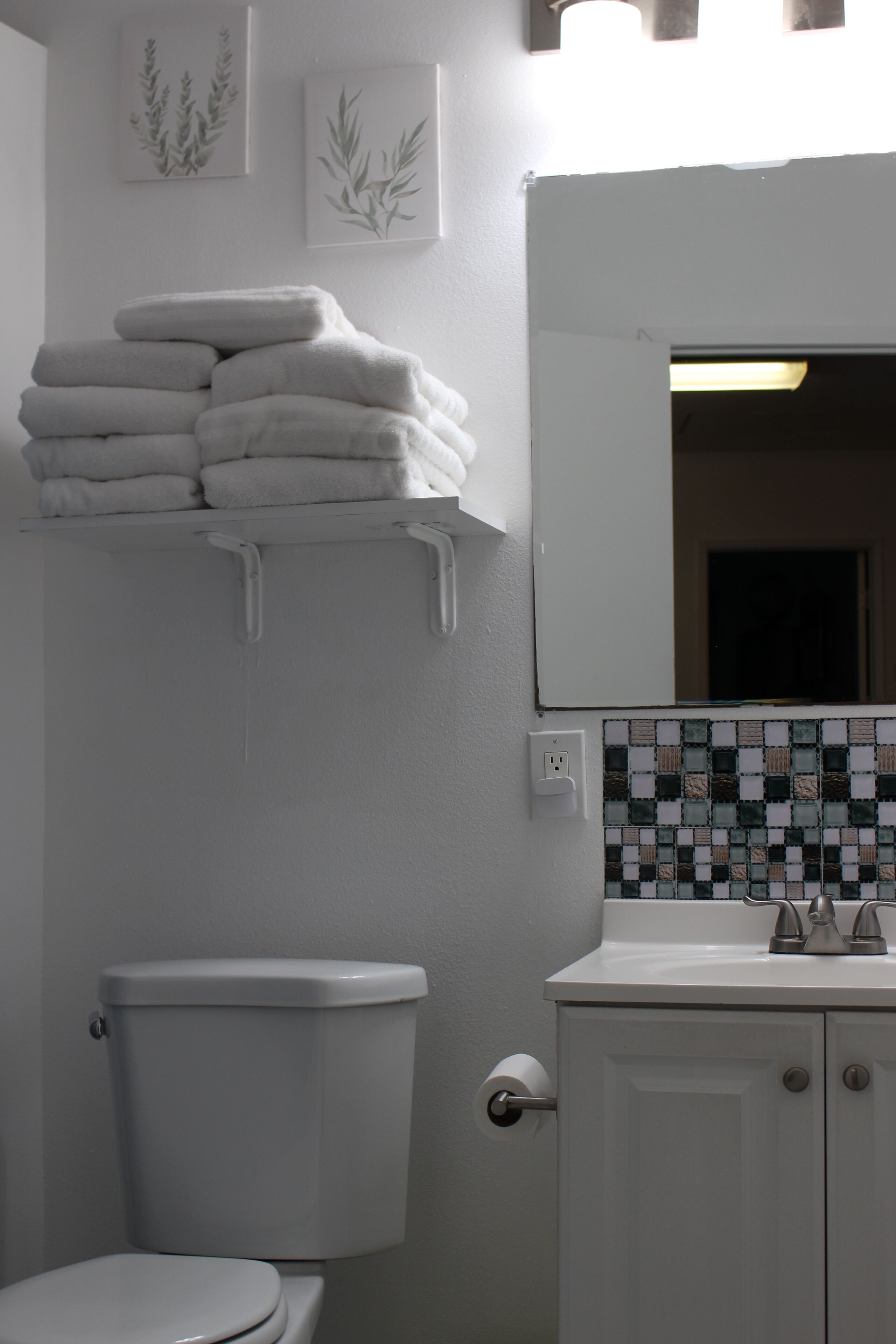 Une salle de bain avec des toilettes, un lavabo, un miroir et une pile de serviettes sur une étagère.