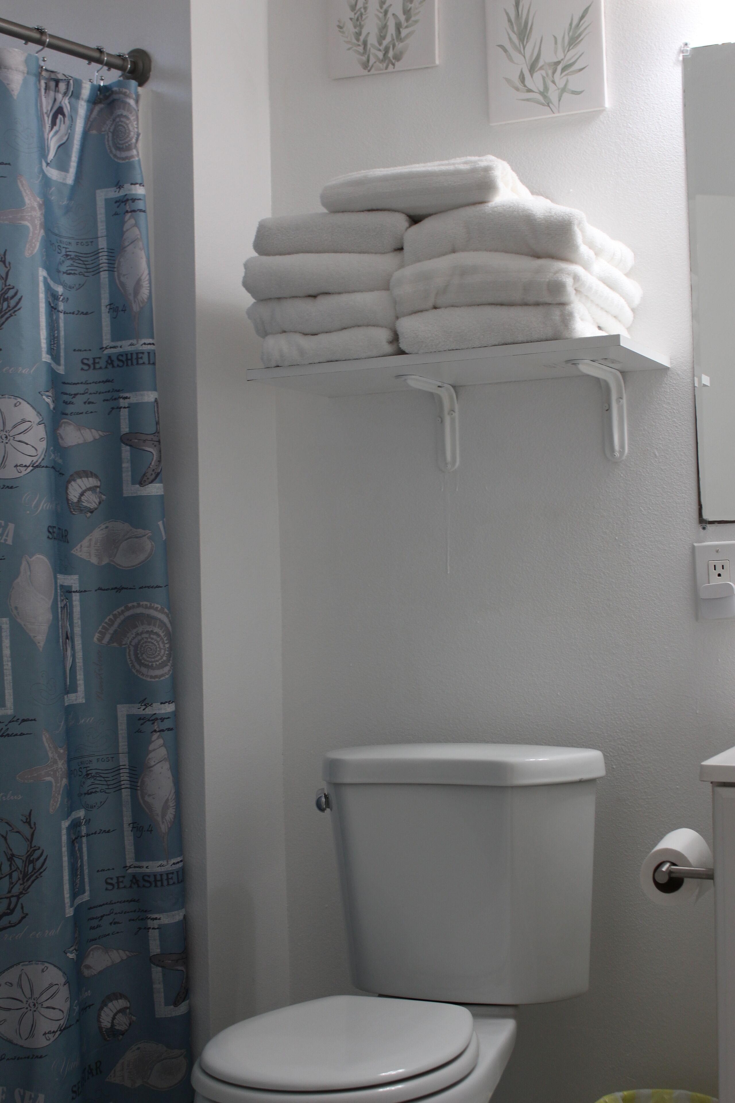 Un baño con inodoro, una pila de toallas blancas y una cortina de ducha azul con motivos marinos.