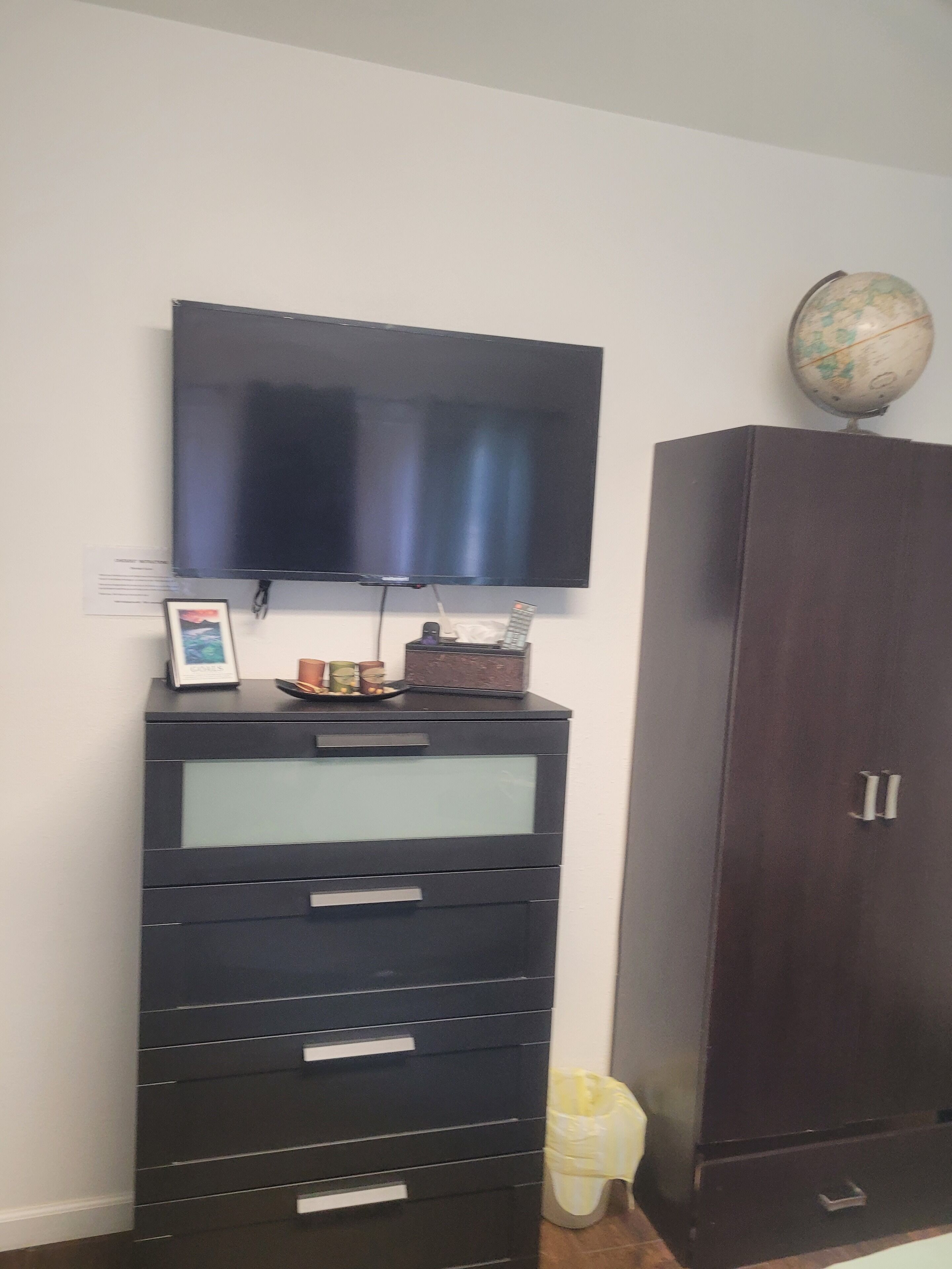 Habitació amb un televisor de pantalla plana penjat a la paret, un moble de fusta fosca i un glob dins del moble.