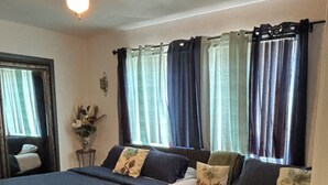 A room with two beds, a ceiling fan, and a window with curtains.