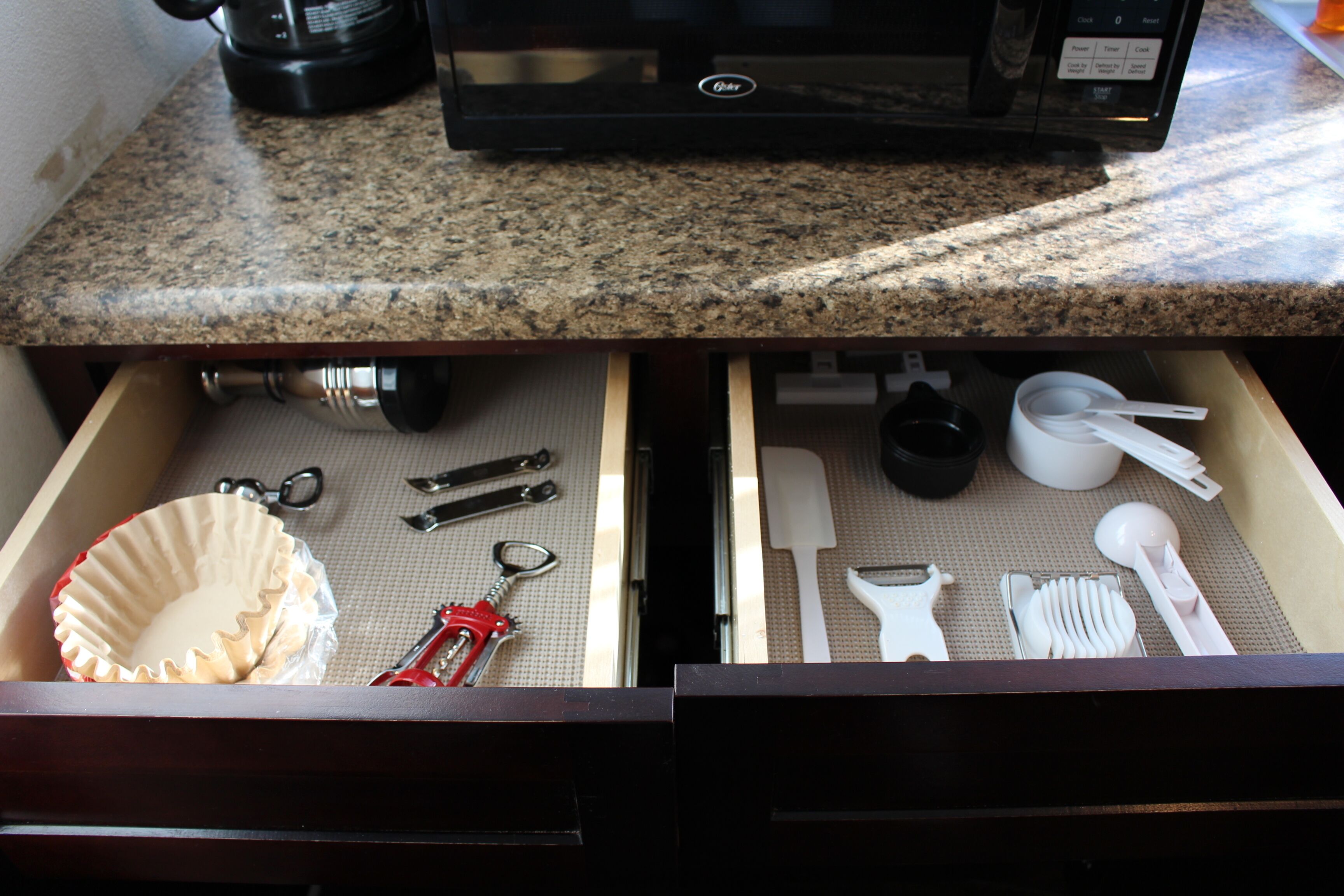 A kitchen counter with a microwave and a drawer containing various utensils and kitchenware.