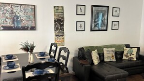 A dining area with a wooden table and chairs, a black sofa, and a wall with framed pictures and a motivational poster.