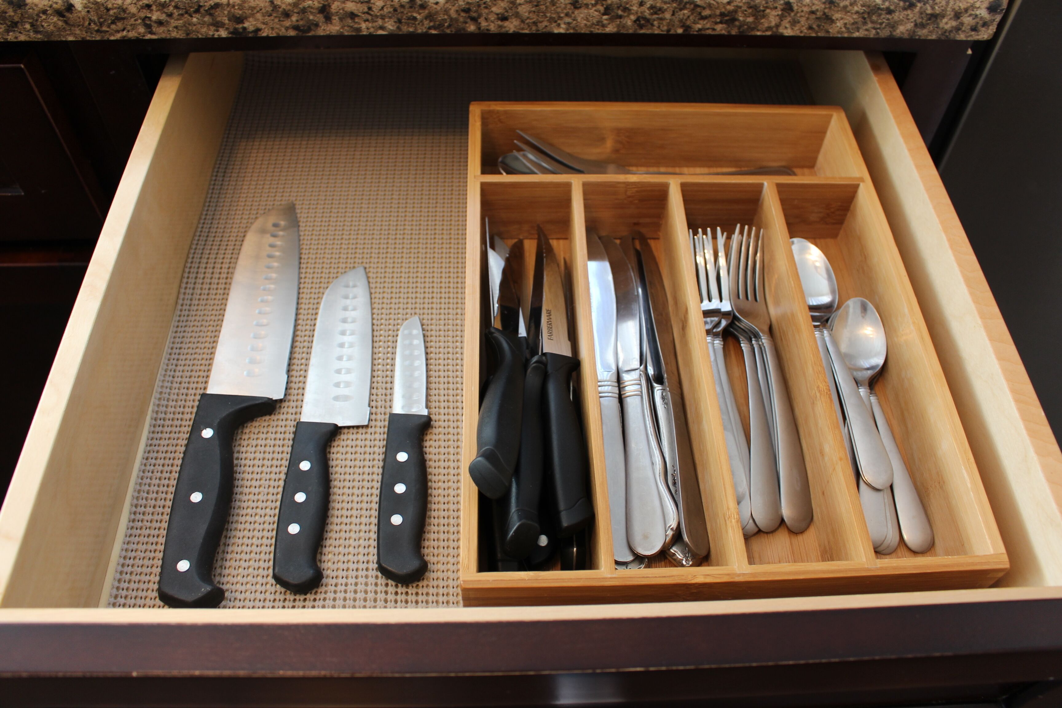 A drawer with various kitchen utensils including knives, forks, and spoons.
