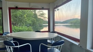 Un comedor con una mesa redonda y sillas azules, ventanas amplias con vistas a un lago y árboles, y una lámpara de techo.