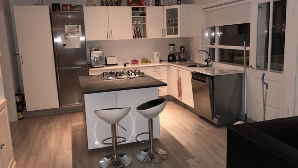 A modern kitchen with white cabinets, a stainless steel refrigerator, a gas stove, and two bar stools. - White house in Hafnafjörður (Hafnarfjordur)