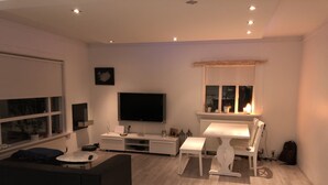 A modern living room with a flat-screen TV, a dining table, and a cozy seating area. - White house in Hafnafjörður (Hafnarfjordur)