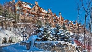 A large, multi-story lodge with a stone facade, multiple balconies, and snow-covered surroundings. - White Altitude | Ski-in/Ski-out Mont-Tremblant | Walk to ski village/Views / Hot tub (Mont-Tremblant)