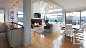 A spacious living area with a fireplace, a dining table, and a view of the outdoors. - White Altitude | Ski-in/Ski-out Mont-Tremblant | Walk to ski village/Views / Hot tub (Mont-Tremblant)