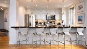 A modern kitchen with stainless steel appliances, a bar area with bar stools, and pendant lighting. - White Altitude | Ski-in/Ski-out Mont-Tremblant | Walk to ski village/Views / Hot tub (Mont-Tremblant)
