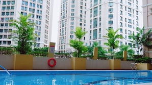 Una piscina con un flotador salvavidas, rodeada por una cerca y palmeras, con edificios residenciales altos al fondo.