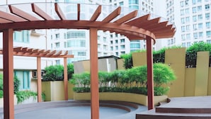 Un espacio exterior techado con una pérgola de madera, rodeado de vegetación y un sendero curvo.