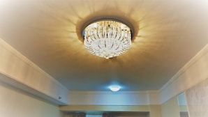 Una habitación con candelabro, luz de techo y ventana con cortinas.