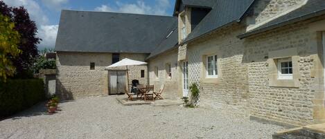 Un bâtiment en pierre avec une cour en gravier, des sièges en plein air et un espace couvert comprenant une table et des chaises.