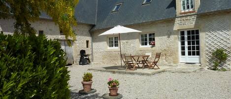 A stone building with a gravel courtyard, outdoor seating, and potted plants.