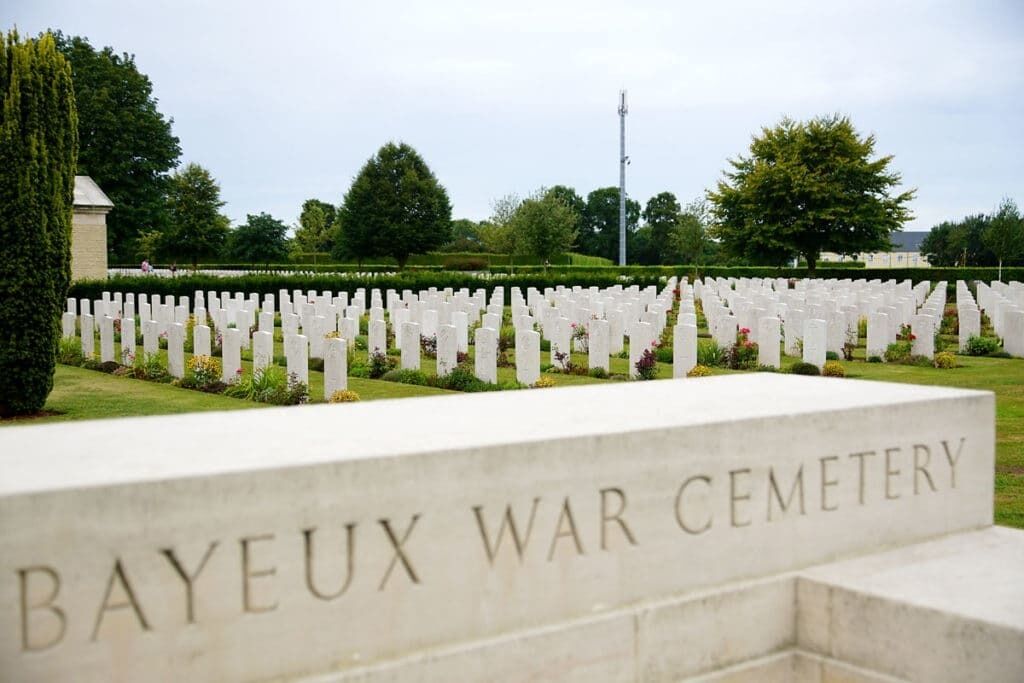 A cemetery with white headstones and a sign that reads "Bayeux War Cemetery".
