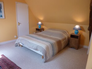 Un dormitorio con cama, dos mesitas de noche con lámparas, una puerta y suelo alfombrado.