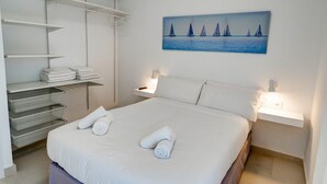 A hotel room with a neatly made bed, a painting of sailboats, and a white wardrobe with shelves. - Sitges with pool near beach by Hello Homes Sitges (Sitges)