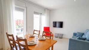 A dining area with a wooden table set for four, a red chair, a blue sofa, and a TV on the wall. - Sitges with pool near beach by Hello Homes Sitges (Sitges)