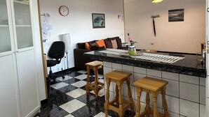 Uma cozinha com chão xadrez, banquetas de madeira, bancada de mármore e iluminação pendente.