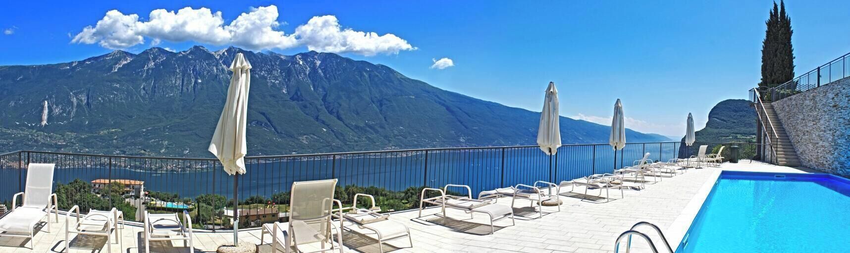 A poolside area with lounge chairs and umbrellas, overlooking a mountainous landscape.