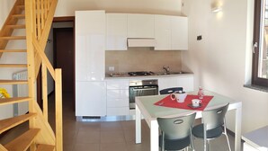 Een moderne keuken met witte kastjes, een eettafel met stoelen en een houten trap.