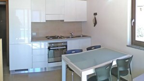 Een compacte keuken met witte kasten, een gasfornuis en een oven. Er is een eettafel met twee stoelen.