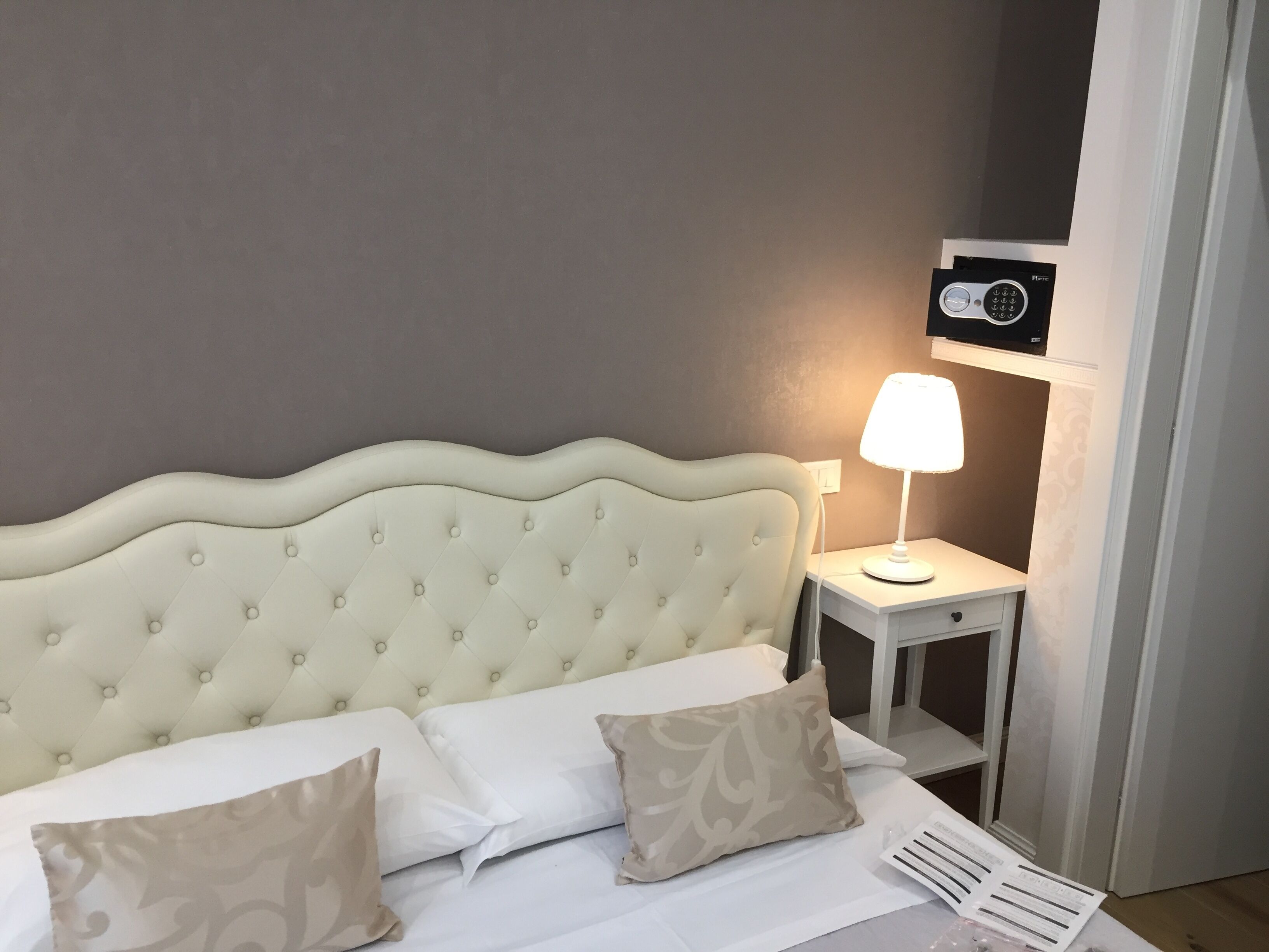 Una cama bien hecha con un cabecero acolchado, una lámpara de noche y una mesita de noche con un control remoto.