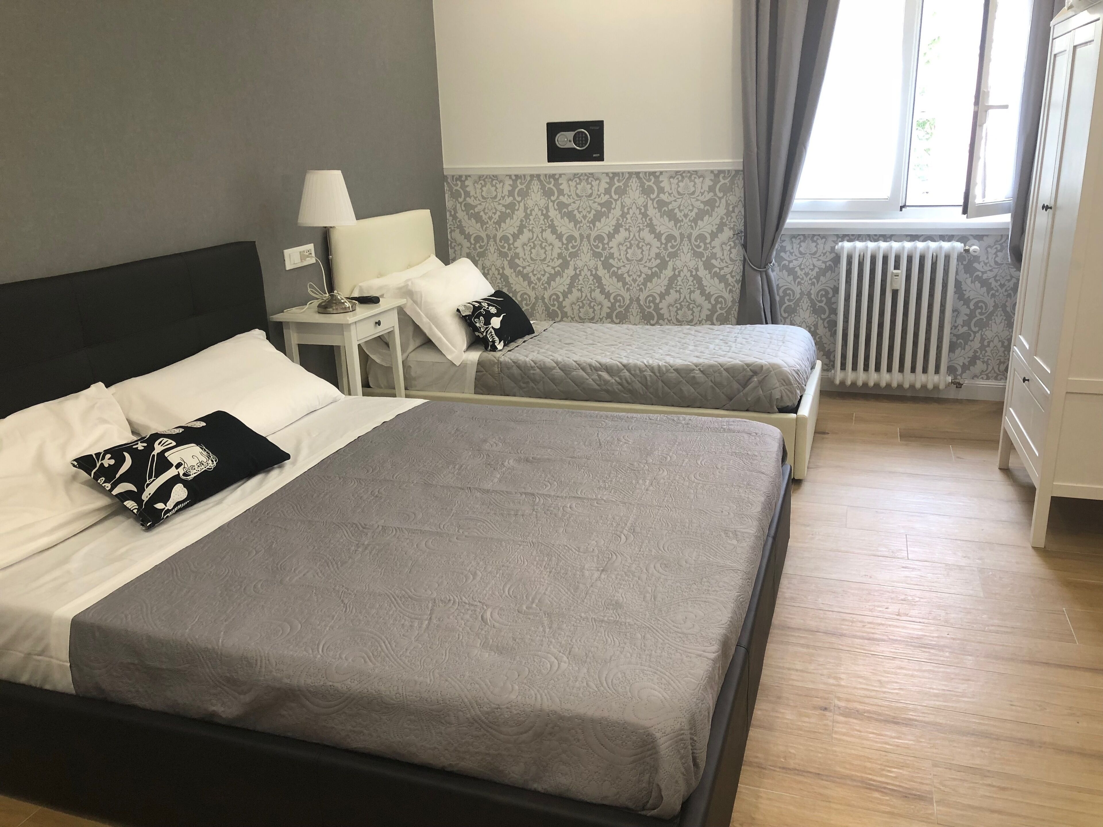 Une chambre d’hôtel avec deux lits, une table de chevet, une lampe, un radiateur et une fenêtre avec des rideaux.