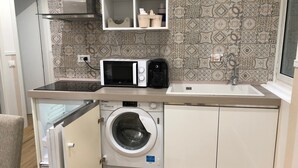 Una cocina compacta equipada con lavadora integrada, microondas y un lavabo.