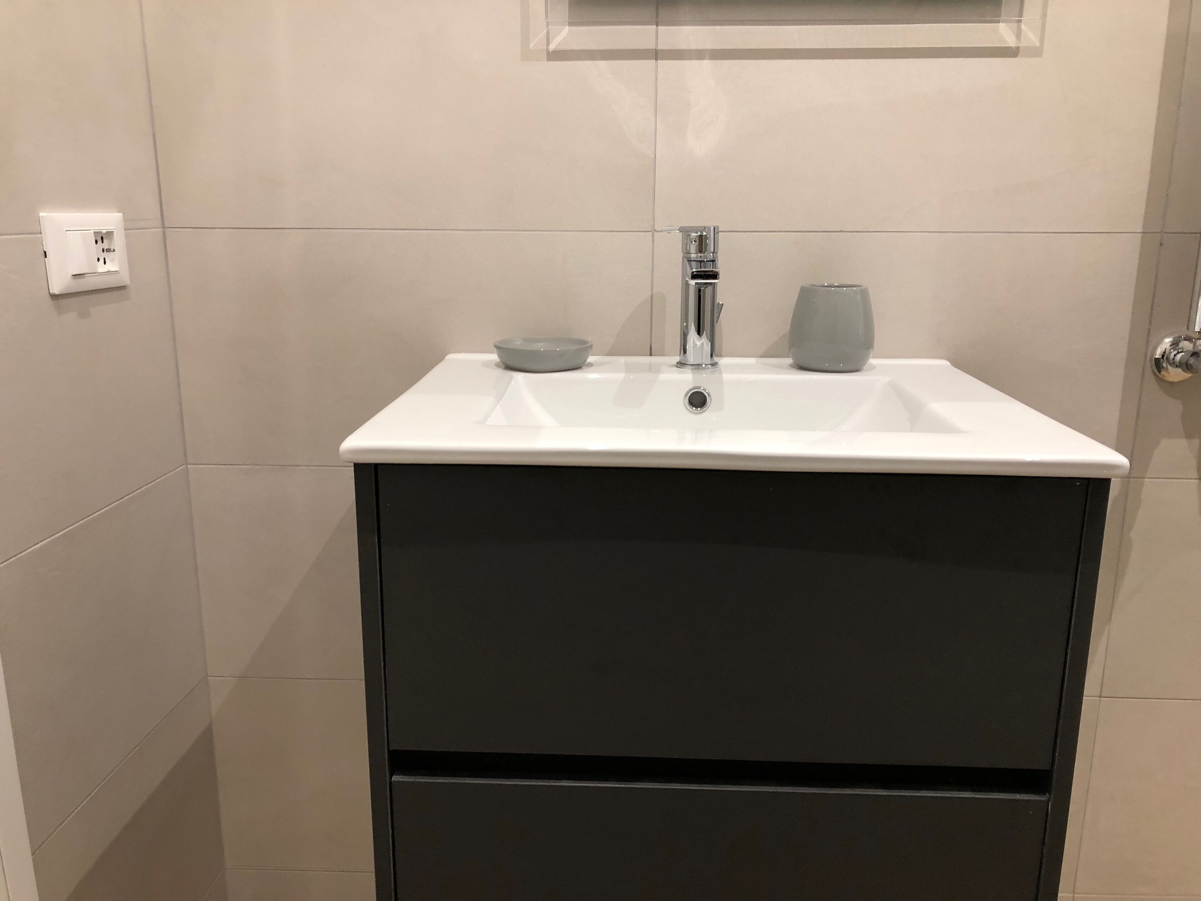 Ein Badezimmer mit einem weißen Waschbecken, einem Spiegel darüber und einem Handtuchhalter zur rechten Seite.