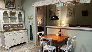 A dining area with a wooden table and white chairs, a cabinet with glass doors, and a patterned rug. - 2 Bedroom & 2 Bathroom Gîte Cottage Heated Plunge Pool & Private Garden 86150 (Le Vigeant)