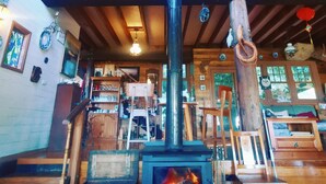 A rustic cabin interior with a central wood-burning stove, wooden beams, a balcony, and a cozy seating area. - The Goat and Goose B&B (Lakes Entrance)