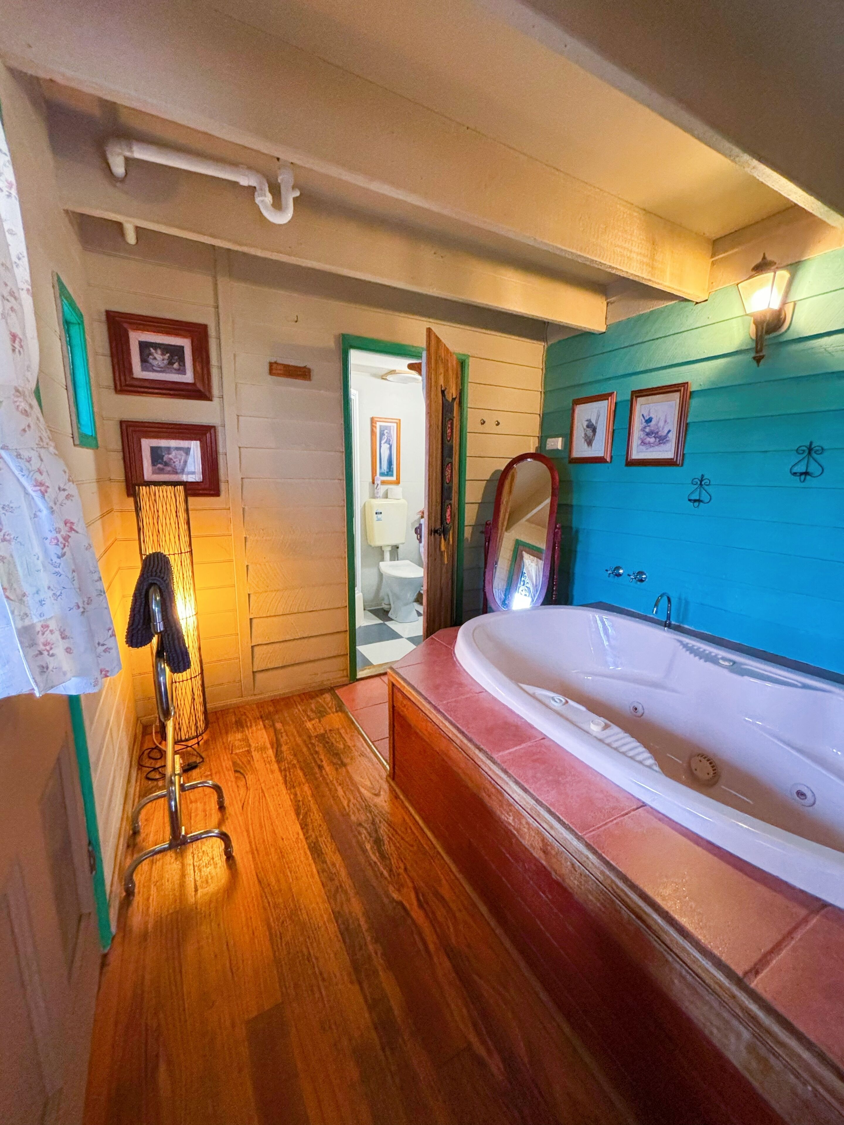 Une salle de bain avec un plancher en bois, une grande baignoire et une porte en bois donnant accès aux toilettes.