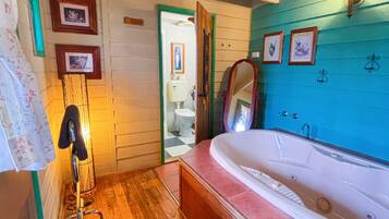Une salle de bain avec un plancher en bois, une grande baignoire et une porte en bois donnant accès aux toilettes.