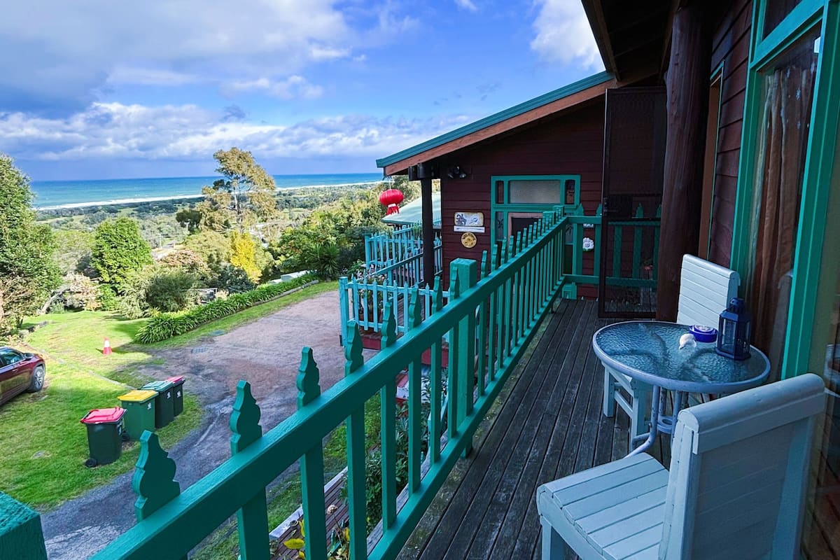 A wooden deck with a view of the ocean, a table with chairs, and a red lantern.