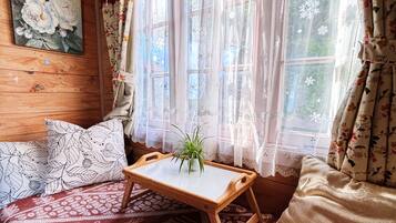 A cozy room with a wooden ceiling, a bed with patterned bedding, a small wooden table with a plant, and a window with floral curtains.
