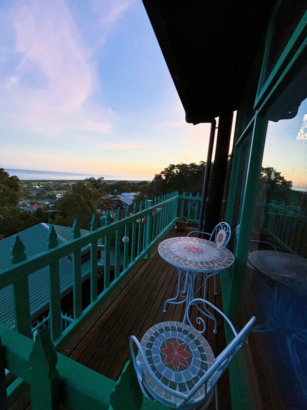 A wooden deck with a green railing, a small table with a mosaic top, and a chair. - The Goat and Goose B&B (Lakes Entrance)