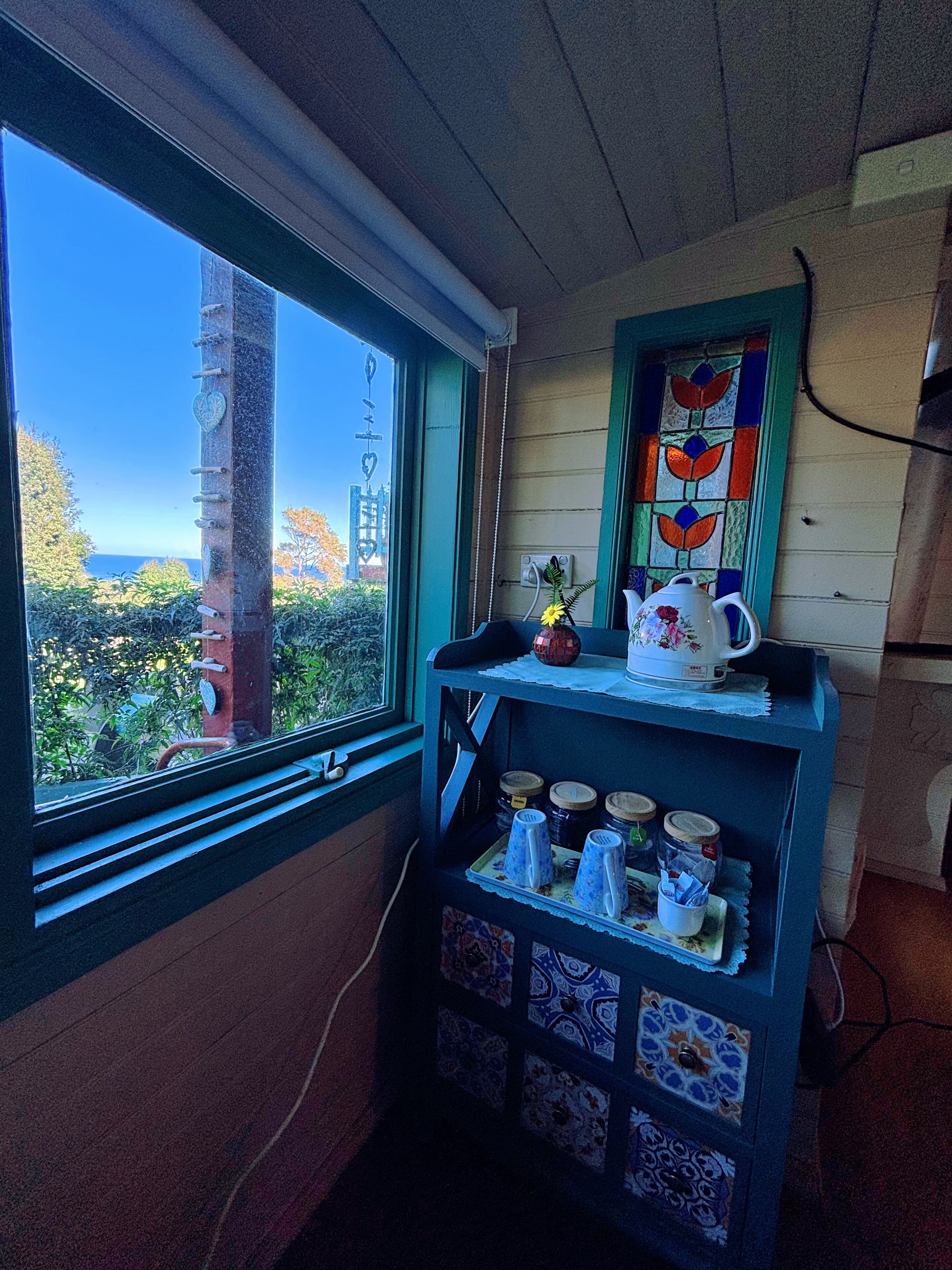 Una habitación con ventana que da a un jardín, una estantería con utensilios de cocina y un adorno en la pared.