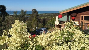 A wooden building with a view of the sea, surrounded by greenery and white flowering plants. - The Goat and Goose B&B (Lakes Entrance)