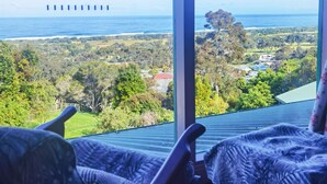A room with a large window overlooking a coastal landscape, including a view of the sea and distant buildings. - The Goat and Goose B&B (Lakes Entrance)