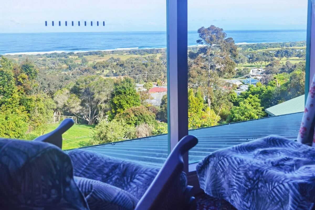 A room with a large window overlooking a coastal landscape, including a view of the sea and distant buildings.