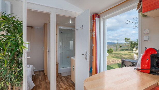 Une salle de bain moderne avec une douche en verre, des toilettes et un lavabo. Le sol est en bois et une porte ouverte donne sur un jardin.