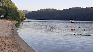Un lac paisible, avec un bateau visible au loin, entouré d’une colline boisée.